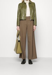 Veste en cuir vert olive, col roulé beige, pantalon évasé marron et grand sac olive. Des bottes noires à chevilles complètent la tenue.