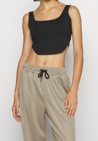 Czarny krótki top na ramiączkach o szerokich paskach i bezszwowym designie. W połączeniu z beżowymi spodniami z troczkami, z mankietami i bocznymi kieszeniami.