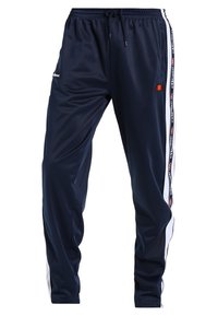 Marina blå träningsbyxor i slät tyg, med vita sidostrikar och en elastisk midja med snörning. Logotyper är synliga.