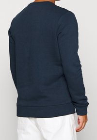 Sudadera azul marino con cuello redondo, puños y dobladillo acanalados, con detalles texturizados en los hombros y una tela suave de mezcla de algodón.