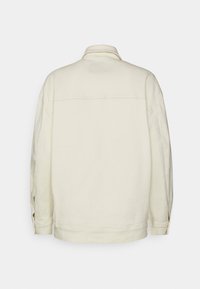 Chaqueta de gran tamaño color crema con cuello clásico, mangas largas y corte recto. Detalles de costura en los hombros y los puños.