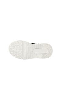 Semelle en caoutchouc blanc avec motif de grip texturé et détail du logo. Partie supérieure noire visible, présentant un design épuré et minimal.