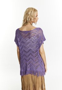 Top de ganchillo morado con patrón en zigzag y dobladillo con flecos. Llevado sobre una falda marrón con flecos, que muestra un diseño de tejido abierto y un ajuste relajado.