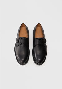 Et par sorte læder monk strap dress sko med sølvspænder, synlig syning og beige indlægssåler på en helt hvid baggrund.