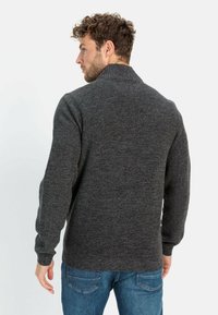 Grauer Strickpullover mit hohem Kragen, gerippter Textur und langen Ärmeln. Über blauen Jeans getragen, von hinten betrachtet.
