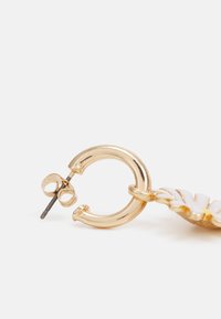 Brinco de argola em ouro com superfície texturizada, apresentando um fecho seguro de pino e acentos decorativos de folhas brancas.