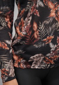 Langermet topp i svart stoff med blomster- og bladmønster i rødt, oransje og grønt. Myk tekstur, kroppsnær fasong.