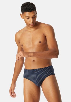 Laivastonsiniset uimahousut valkoisilla pinstripes-kuvioilla, joustavalla vyötärönauhalla ja istuvalla mallilla. Materiaali näyttää sileältä ja hieman kiiltävältä.