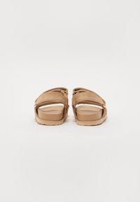 Beige schuifsandalen met quilted textuur, twee brede banden en een massieve rubberen zool. Eenvoudig ontwerp, ronde neus en een gladde afwerking.