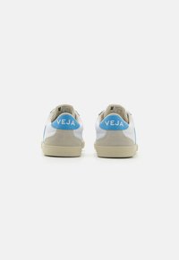 Hvite og beige sneakers med blå detaljer. Har en glatt skinn øvre, suehæl og gummisåle med et teksturert mønster.