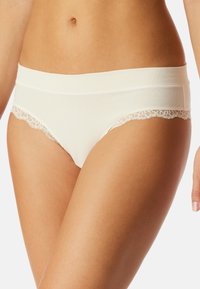Sous-vêtements de couleur crème avec un devant lisse et une finition en dentelle le long des jambes, présentant un design taille basse et une texture douce.