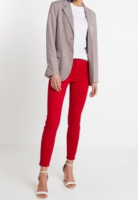 Blazer grigio a scacchi con rever a punta sopra una t-shirt bianca, abbinato a jeans skinny rossi e sandali bianchi con cinturini.