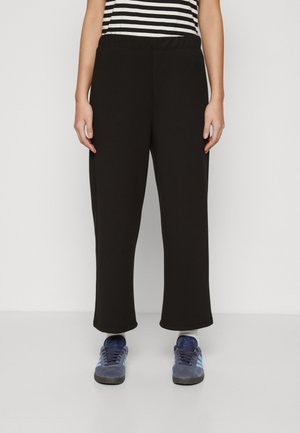 Black sweatpants with an elastic waistband, wide-leg design, smooth texture, paired with blue athletic shoes featuring light blue accents.