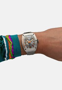 Silver stainless steel watch with a textured gray dial, orange accents, bold hour markers, and a smooth link bracelet, worn on a wrist.