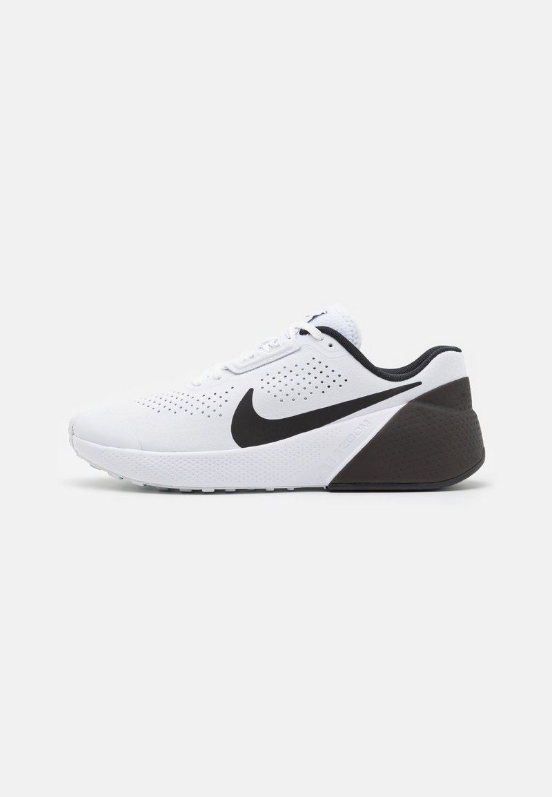 Chaussure de sport blanche avec un dessus perforé, logo Nike swoosh noir et un talon noir texturé. Conception légère avec un système de laçage.