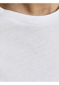 Camiseta de algodón blanca, con una textura suave y un cuello redondo acanalado. La vista en primer plano destaca el fino tejido de la tela y su apariencia ligera.