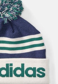 Gorro de malha em azul marinho com riscas brancas e verdes. Apresenta um pom-pom fofinho no topo e o logótipo "adidas" em verde na bainha.