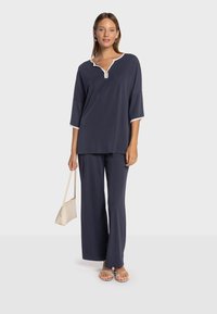 Ensemble deux pièces bleu marine comprenant un haut ample avec un col blanc et des manches aux trois quarts, associé à un pantalon à jambes larges. Design simple et moderne.
