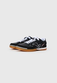 Chaussures de sport noires avec des lacets blancs, en matériau synthétique texturé, semelle en caoutchouc gomme et un accent logo blanc sur le côté.