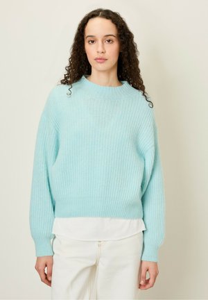 Lichtblauwe gebreide trui met een geribbelde textuur, ronde halslijn en een losse pasvorm. Draag je over een wit shirt, mouwen zijn iets omgeslagen.