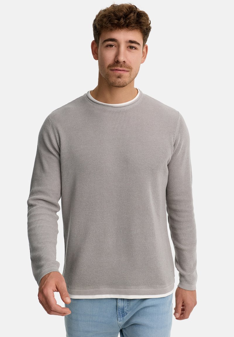Suéter gris de tejido waffle con mangas largas y cuello redondo, que presenta un dobladillo y puños en blanco contrastante. El modelo usa jeans de color azul claro.