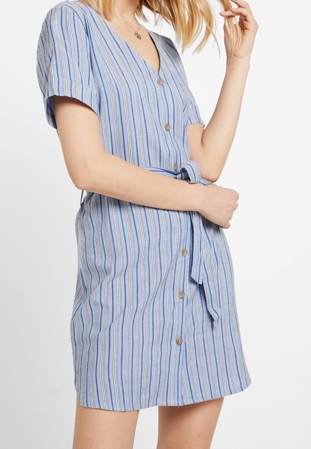 Femme portant une robe bleue à rayures, à manches courtes, boutonnée à l'avant, avec une ceinture en tissu nouée à la taille, sur un fond blanc.