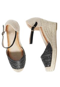 Espadrille con zeppa intrecciata nera e punta intrecciata beige, dotata di una fascia nera alla caviglia e di una suola in corda texturizzata.
