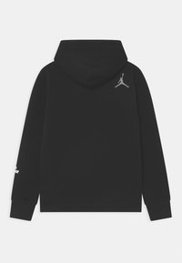 Felpa nera vista da dietro con un piccolo logo Jumpman grigio in alto a destra e testo bianco sul polsino sinistro.