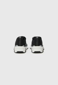 Chaussures de sport noires avec accents gris, présentant un dessus en maille texturée, une semelle blanche rembourrée et une languette à l'arrière pour un enfilage facile.