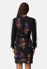 Black floral dress with polka dots, sheer sleeves, waist tie, and layered ruffle hem. Features multicolored flowers and lace trim.