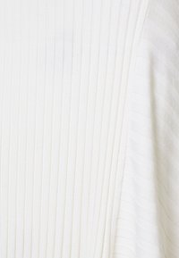 Bílá žebrovaná textilie s vertikálními pruhy a jemně strukturovaným povrchem, vytvářející nepatrný vzor na látce.