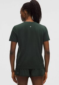 Camiseta deportiva de manga corta de color verde oscuro con una tela texturizada, que presenta un escote redondeado y un logo en la parte superior de la espalda.