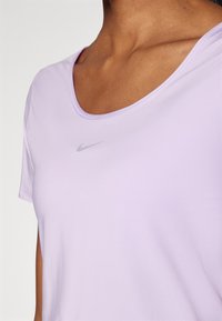 Svetlofialová Nike tričko s okrúhlym výstrihom, krátkymi rukávmi a malým strieborným logom na hrudi. Hladká, ľahká tkanina.