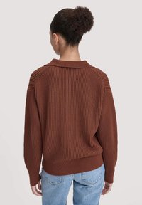 Braun gestreifter Strickpullover mit Kragen, mit fallenden Schultern und langen Ärmeln, kombiniert mit hellblauen Jeans.