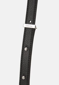 Schwarzer Leder-Gürtel mit strukturiertem Finish, silbernen Hardware-Akzenten und einer geprägten Metallplatte mit "Calvin Klein".