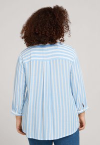 Camisa de botones a rayas en azul claro y blanco con un dobladillo redondeado, un yugo y mangas con tabla para enrollar. Tejido suave con rayas verticales.