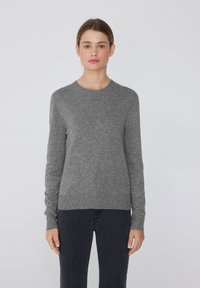 Grauer Strickpullover mit langen Ärmeln und rundem Halsausschnitt, mit glatter Textur und leicht taillierter Form. Kombiniert mit dunklen Jeans.