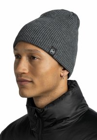 Gray ribbed beanie with a tapered shape, featuring a small black logo tag. Worn with a black, high-collared puffer jacket. Smooth texture.