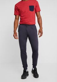 Rödprickig t-shirt med rund halsringning och en marinblå ficka, kombinerad med mörkgrå tapered sweatpants. Bärs med svarta sportskor.