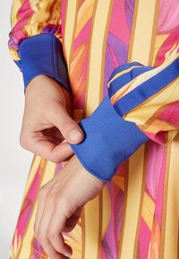 Colorful dress featuring a vibrant floral pattern in pink and yellow, with a blue ribbed cuff at the sleeve, textured fabric detail visible.