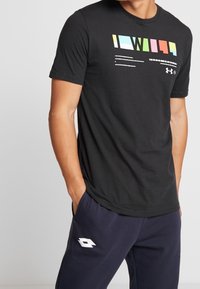 Svart t-shirt med kort ärm som har en färgglad grafisk design på framsidan. Materialet verkar vara mjukt med en klassisk rund hals.