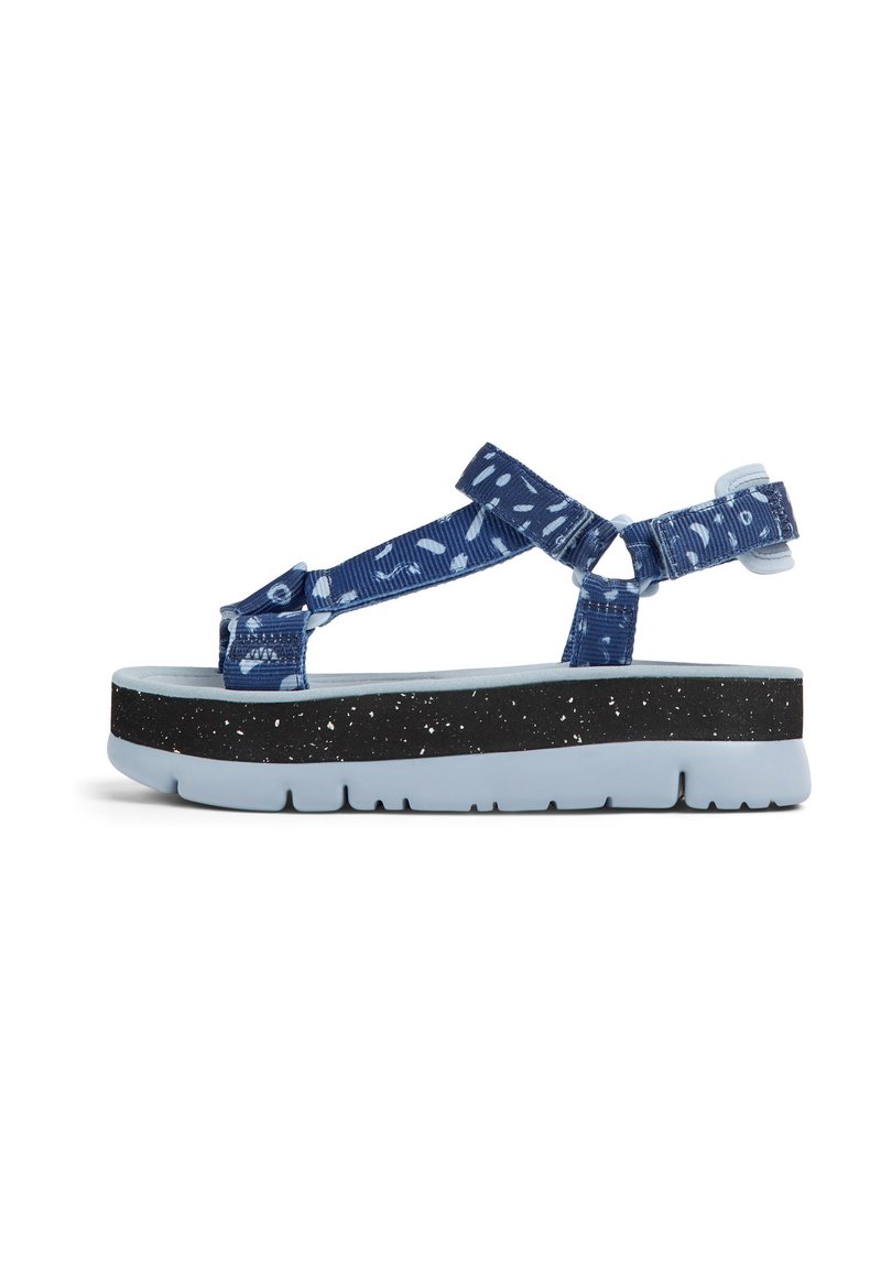 Blå mönstrade sandaler med justerbara remmar, en kraftig svart fläckig sula och en ljusblå fotbädd. Sidan visar design och material.