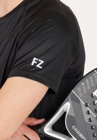 Svart träningsskjorta med slät yta, med vitt "FZ"-logotyp på ärmen. En mönstrad paddelracket hålls mot armen.