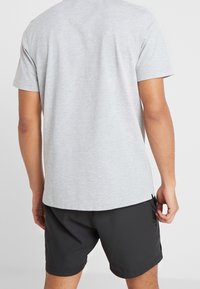 Ljust grå kortärmad t-shirt i mjukt tyg, i kombination med svarta shorts med sidofickor och en mjuk yta.