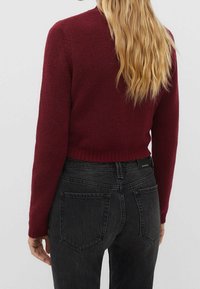 Burgundy cropped sweater with a soft texture, ribbed hem, and round neckline, paired with black high-waisted jeans featuring back pockets.