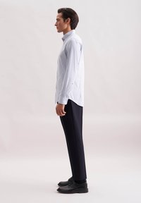 Camicia a maniche lunghe azzurra a quadri abbinata a pantaloni scuri e scarpe nere; presenta un colletto con bottoni e un design aderente.