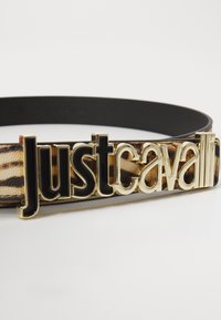 Kovina s sponko v črni in zlati barvi z logotipom "Just Cavalli". Tkanina prikazuje svetlo rjavo vzorčenje, s črnim gladkim usnjenim pasom.