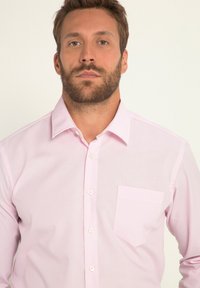 Lichtroze overhemd met knopen en een klassieke kraag, enkele borstzak en witte knopen. Glad stof met een subtiele glans.