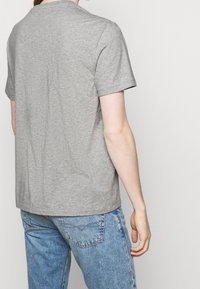 Šedé bavlněné tričko s kulatým výstřihem a krátkými rukávy, s jednoduchým designem a pohodlným střihem, v kombinaci se světle modrými džínami.