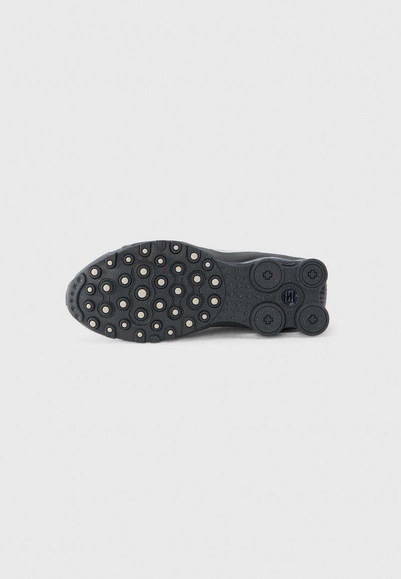 Black sneaker outsole with rounded lugs and circular cutouts, featuring a textured surface and subtle branding on the heel area.